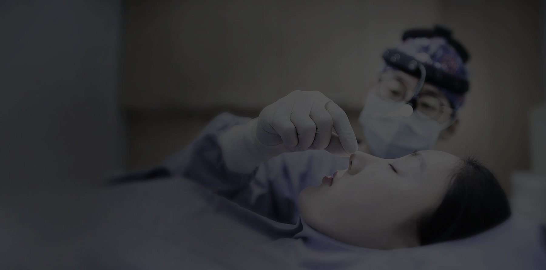 의사가 누운 환자의 코끝을 살펴보는 장면(어두운 톤)